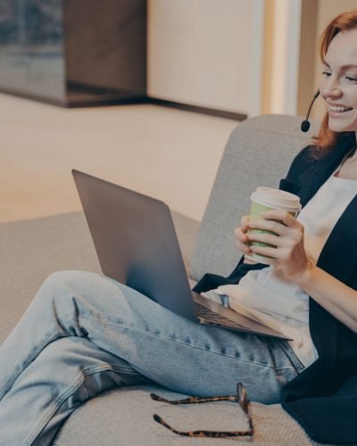 Happy millenial woman wearing headphones and smiling while watching online webinar course on laptop